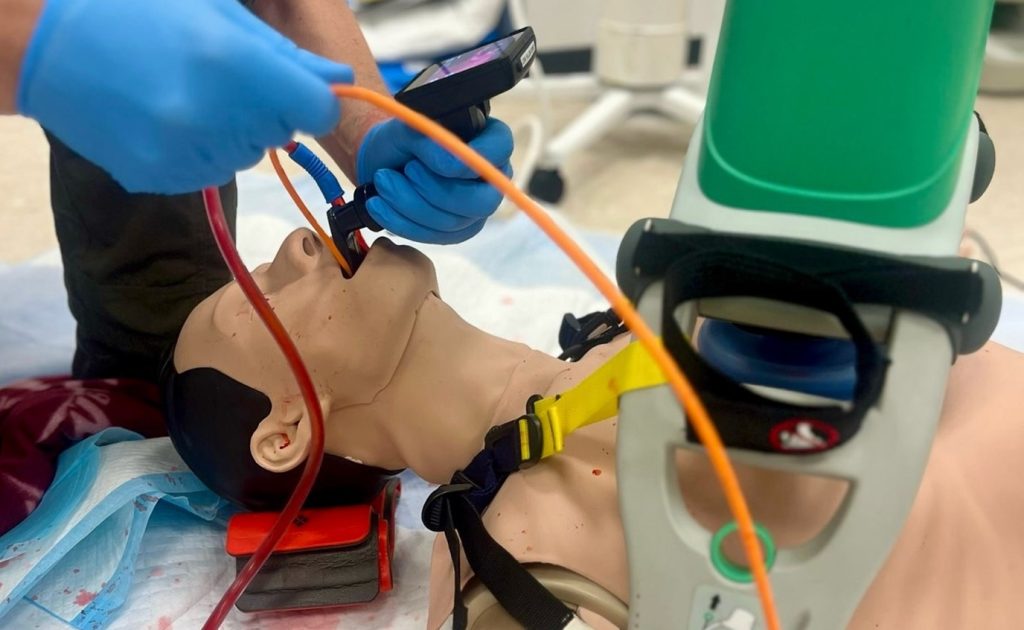 SALAD-Training unter laufender mechanischer Thoraxkompression, Sauger „parkt“ links neben Laryngoskopspatel.