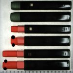 Abb. 1: Fotodarstellung der beiden Seitenansichten des in dieser Studie untersuchten Autoinjektors (lange Seite, kurze Seite) in seinen verschiedenen Zuständen: Die stabile Ausgabeform des Autoinjektors (oben), der auslösebereite Autoinjektor nach Abziehen der Kappe (Mitte) sowie der ausgelöste Autoinjektor nach Abschluss der Anwendung (unten). Der orangefarbene Nadelschutz umschließt die Nadel und verringert die Verletzungsgefahr. Das kennzeichnungslose, hochglänzende Etikett ist nur als Muster aufzufassen und stellt nicht den Endzustand dar. (Bildinhalte wurden aus patentrechtlichen Gründen teilweise unkenntlich gemacht)